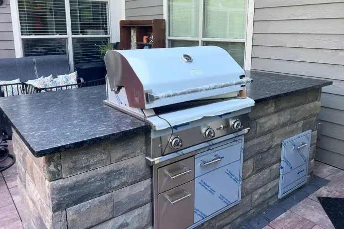 Built-in gas grill installation on custom stone masonry with polished black granite counters