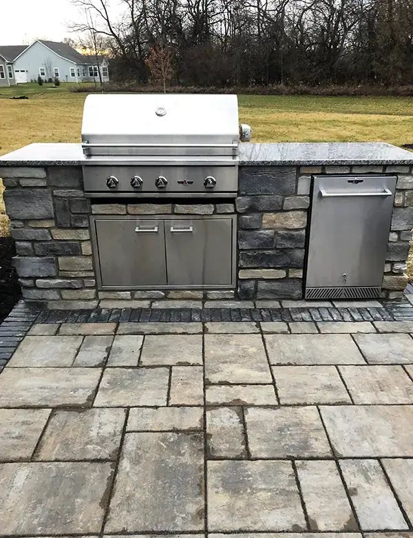 Rustic stone veneer outdoor kitchen with built-in gas grill and natural stone patio